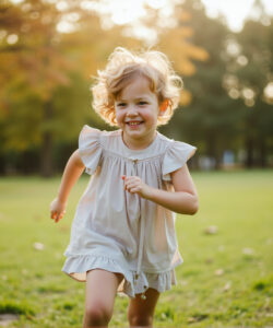 Photograph-of-a-joyful-young-girl-with-curly-blonde-hair-in-a-white-dress-running-in-a-sunlit-park
