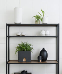 Photograph-of-a-minimalist-black-metal-shelf-with-potted-plants-white-shoes-and-black-ceramics-against-a-white-tiled-wall