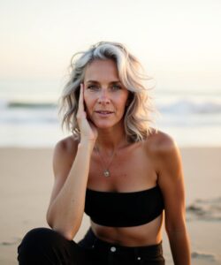 The-photograph-captures-a-woman-sitting-on-a-sandy-beach-during-what-appears-to-be-either-sunrise-or-sunset-as-indicated-by-the-soft-warm-lighting-and-the-gentle-pastel-hues-of-the-sky-She