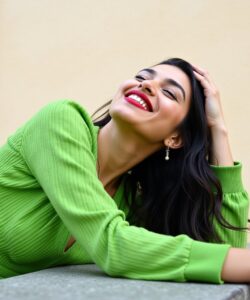 The-photograph-captures-a-young-woman-with-long-dark-hair-cascading-over-her-shoulders-leaning-against-a-light-yellow-wall-She-has-a-warm-olive-toned-skin-and-a-radiant-smile-her-eyes