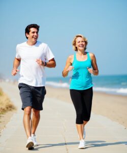 This-is-a-photograph-of-two-people-a-man-and-a-woman-walking-together-on-a-sandy-beach-The-man-is-on-the-left-wearing-a-white-t-shirt-gray-shorts-and-white-sneakers