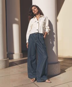 a-woman-standing-in-a-modern-minimalist-architectural-setting-The-scene-is-bathed-in-natural-sunlight-casting-long-shadows-on-the-beige-walls-and-floor-The-woman-is-1