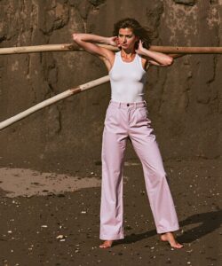 a-woman-standing-on-a-sandy-beach-with-a-rugged-rocky-cliff-as-the-backdrop-She-is-positioned-slightly-off-center-facing-the-camera-with-her-arms-raised-and-hands-resting-on-the-top