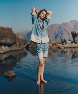 a-young-woman-standing-in-a-shallow-clear-pool-of-water-surrounded-by-rugged-rocky-terrain-and-majestic-mountains-under-a-clear-blue-sky-The-woman-is-Caucasian-with-light-brown-hair