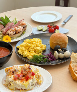 A-photograph-of-a-light-wooden-table-set-with-a-meal-featuring-shrimp-salad-bread-and-a-glass-of-water