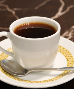 A-photograph-of-a-white-cup-with-dark-coffee-on-a-yellow-trimmed-saucer-placed-on-a-marble-table