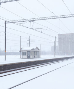 A-serene-snow-covered-train-station-with-empty-tracks-a-small-shelter-and-overcast-skies-featuring-electric-poles-and-wires