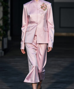 A slender model in a pale pink satin suit with floral embroidery walks on a runway photographed by ap