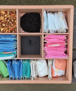 A-top-down-photograph-of-a-wooden-compartment-box-containing-assorted-menstrual-products-nuts-and-a-tea-bag