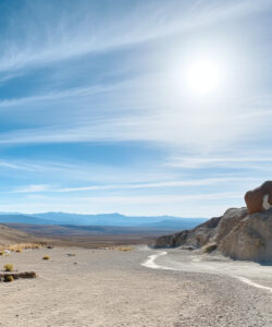 A-vivid-photograph-of-a-sunlit-desert-landscape-with-a-winding-path-rugged-rock-formations-and-distant-mountains