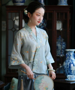 A young asian woman in traditional chinese attire holding a fan stands in a dimly lit room with blue vases