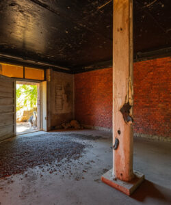 Abandoned-brick-room-with-open-door-scattered-wood-chips-and-exposed-ceiling-beams-rustic-neglected-ambiance-Photograph