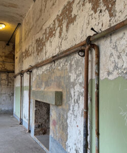 Abandoned-peeling-painted-corridor-with-rusty-pipes-green-and-white-walls-and-a-dimly-lit-doorway-leading-to-a-shadowy-room