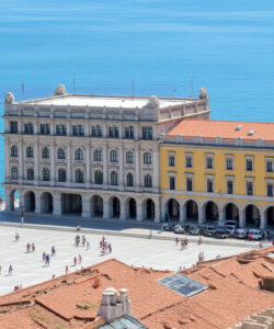 Aerial-photograph-of-Lisbon-s-Praca-do-Comercio-with-colorful-buildings-sailboat-and-people-vibrant-blue-sky-and-ocean-backdrop