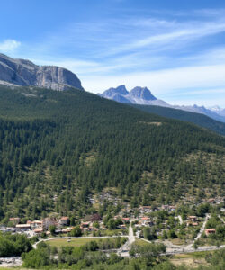 Aerial-photograph-of-a-lush-green-valley-with-dense-forests-a-small-village-and-snow-capped-mountains-under-a-clear-sky