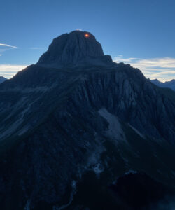 Aerial-photograph-of-a-rugged-snow-capped-mountain-peak-at-sunrise-with-a-glowing-orange-light-near-the-summit