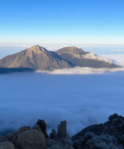 Aerial-photograph-of-a-snow-covered-mountain-peak-with-surrounding-clouds-and-clear-blue-sky