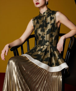 Asian woman in a sleeveless camo patterned dress with a pleated skirt sitting on a black chair studio lighting