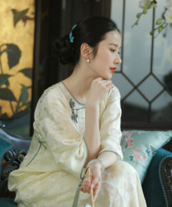 Asian woman in traditional chinese dress sitting on a teal couch looking to the side delicate features elegant setting
