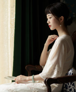 Asian woman in white dress reading book by window dark green curtains elegant soft lighting watermark
