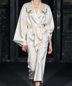 Asian woman wearing a white kimono with floral embroidery walking on a dark runway photograph fashion show medium shot