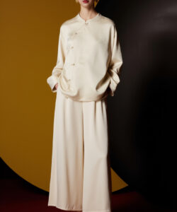 Asian woman wearing cream silk robe and matching wide leg pants standing against a black and yellow circular background