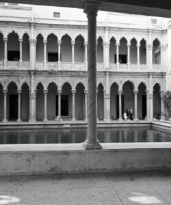 Black-and-white-photograph-of-a-Venetian-courtyard-with-arched-columns-detailed-stone-carvings-and-a-central-fountain