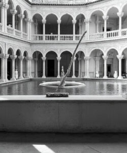 Black-and-white-photograph-of-ornate-courtyard-with-columns-arches-and-a-central-fountain-featuring-intricate-carvings-and-a-symmetrical-design