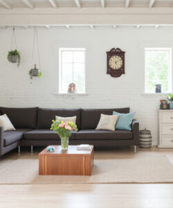Bright-minimalist-living-room-with-a-dark-sectional-sofa-wooden-coffee-table-potted-plants-white-brick-walls-and-soft-lighting