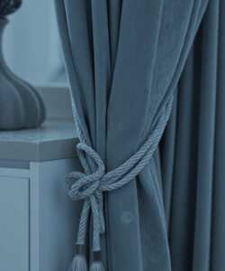 Close-up-photograph-of-a-grey-blue-draped-curtain-tied-with-a-rope-on-a-light-colored-countertop-with-a-vase