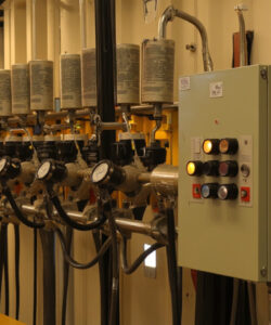 Industrial-control-panel-with-multiple-valves-pressure-gauges-and-switches-set-in-a-beige-metal-walled-room-featuring-yellow-piping