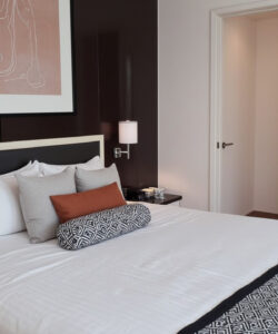 Modern-bedroom-photograph-featuring-a-neatly-made-bed-with-white-linens-brown-accent-wall-and-abstract-art-above
