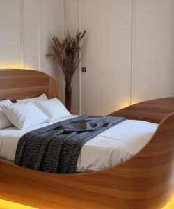 Modern-bedroom-with-a-unique-curved-wooden-bed-white-bedding-grey-throw-soft-ambient-lighting-and-tall-windows