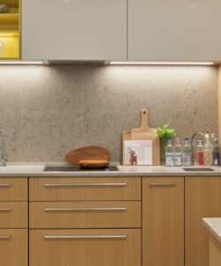 Modern-kitchen-with-light-wood-cabinets-granite-countertops-stainless-steel-appliances-and-a-yellow-lit-open-shelf