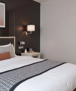 Modern-minimalist-bedroom-photograph-featuring-a-neatly-made-bed-with-grey-and-white-pillows-a-dark-accent-wall-and-artwork
