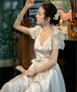 Photo of an asian woman in a white dress sitting elegant floral arrangement lace indoor setting watermark