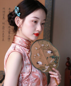 Photo of an asian woman with fair skin wearing a pink silk cheongsam holding a traditional fan red lips elegant