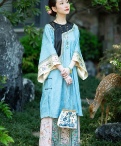Photograph asian woman in traditional blue and pink floral robe holding vintage bag standing near deer in lush garden