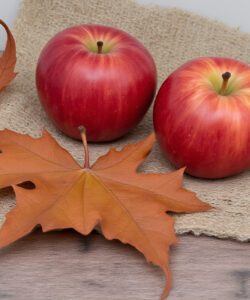 Photograph-Two-red-apples-two-orange-maple-leaves-on-a-beige-burlap-square-wooden-surface-background