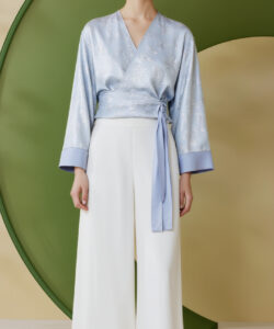 Photograph of asian woman with fair skin wearing light blue and white kimono style top white pants and hoop earrings