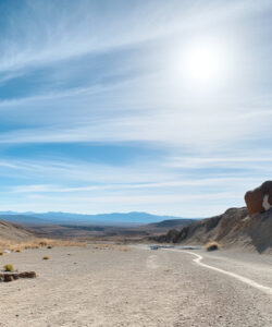 Photograph-of-a-barren-arid-desert-landscape-with-a-winding-dirt-road-under-a-bright-clear-blue-sky