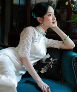 Photograph of a beautiful slender asian woman in a white lace dress seated on a teal sofa in an elegant room