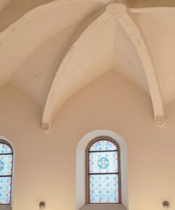 Photograph-of-a-beige-vaulted-ceiling-with-three-arched-stained-glass-windows-showcasing-intricate-blue-and-red-patterns