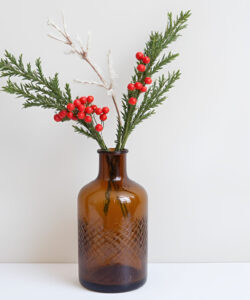 Photograph-of-a-brown-glass-vase-with-red-berries-and-greenery-on-a-plain-white-background