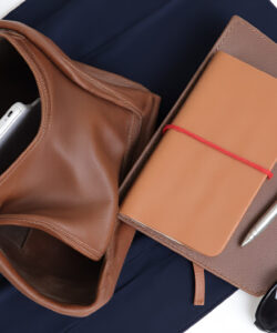 Photograph-of-a-brown-leather-backpack-tan-leather-notebook-and-black-sunglasses-on-navy-fabric