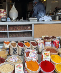 Photograph-of-a-bustling-spice-market-stall-with-vibrant-assorted-grains-and-spices-in-burlap-sacks-featuring-a-vendor