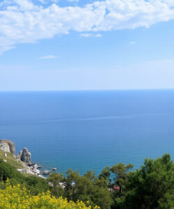 Photograph-of-a-coastal-landscape-featuring-a-historic-stone-building-lush-greenery-and-a-small-island-in-a-blue-sea