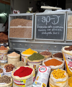Photograph-of-a-colorful-spice-market-stall-with-neatly-arranged-bags-of-grains-beans-and-spices-Italian-text-overhead