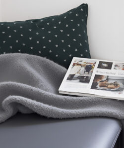 Photograph-of-a-cozy-corner-with-a-gray-blanket-dark-green-pillow-magazine-and-potted-plant-on-a-windowsill