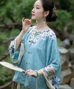 Photograph of a delicate asian woman in traditional blue and white chinese attire holding a fan with greenery background